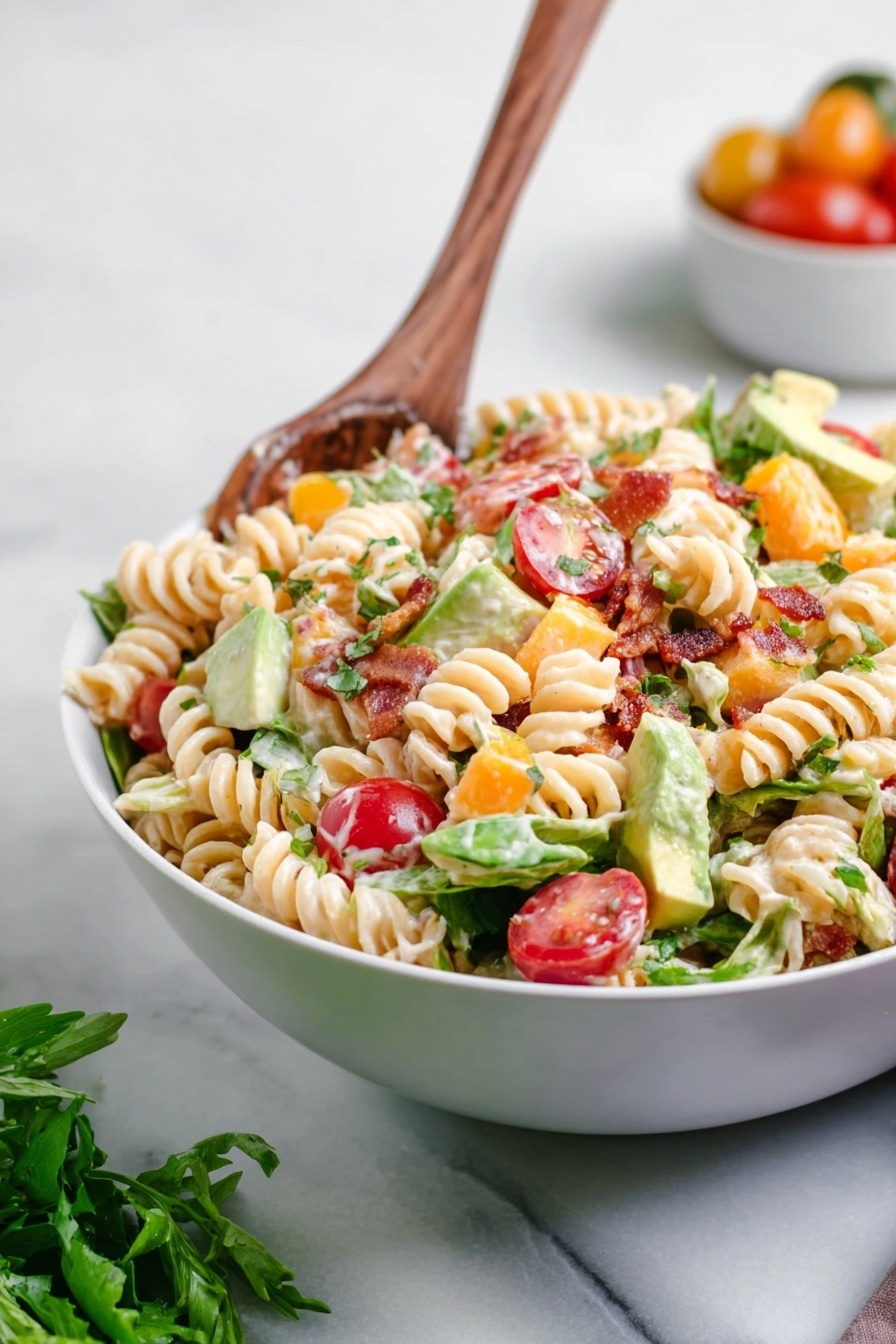 A white bowl filled with a colorful pasta salad sits on a white marbled surface. The salad has three main layers: a base of creamy spiral pasta in light beige, topped with bright red halved cherry tomatoes scattered evenly, and mixed green leafy lettuce pieces adding texture. Small orange cubes of cheddar cheese and light green avocado chunks are mixed throughout. Crispy brown bacon bits sprinkle the salad, along with finely chopped herbs adding green flecks. A wooden spoon is placed inside the bowl with its handle pointing upward, ready to serve. In the background, blurred fresh green herbs and a small white bowl with cherry tomatoes can be seen. Photo taken with an iphone --ar 2:3 --v 7