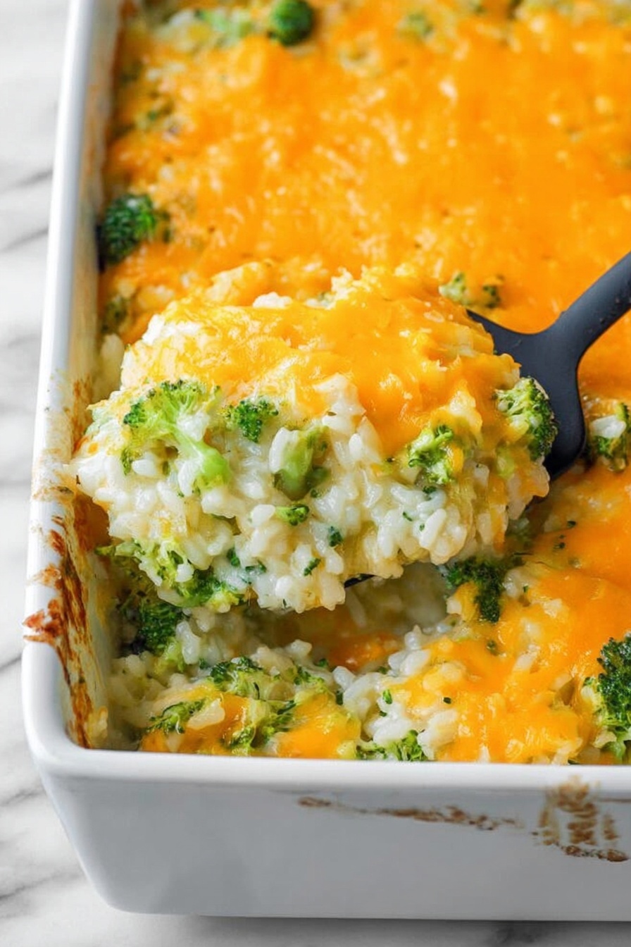 The dish is a baked casserole in a white rectangular dish, with a bright orange melted cheese layer on top. Below the cheese, there is a mixture of white rice and green broccoli pieces visible, giving the dish a textured look with small chunks of vegetables spread throughout. The cheese on top is smooth and slightly bubbly, covering the entire surface except where a black spatula lifts a portion, revealing the creamy, mixed layers underneath. The edges of the casserole dish show some browned spots where the cheese has baked slightly. The background surface is a white marbled texture. Photo taken with an iphone --ar 2:3 --v 7