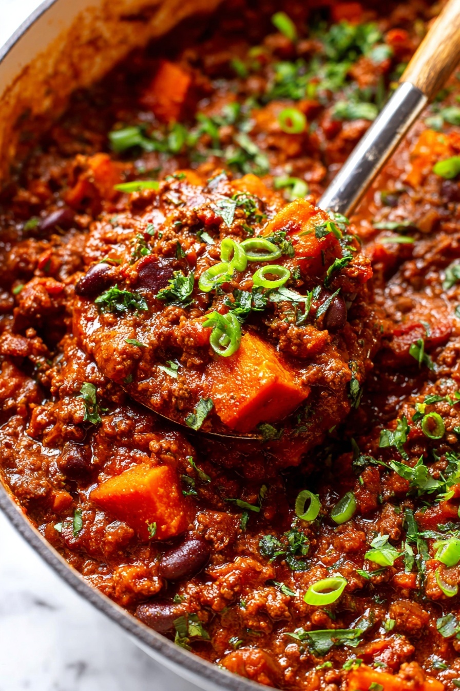 The image shows a close-up of a thick, rich stew filled with chunky pieces of orange sweet potatoes and browned ground meat, all mixed in a deep reddish-brown sauce. Bright green chopped herbs and sliced green onions are sprinkled on top, adding fresh color and texture. The stew is inside a white pot, and a large spoon is scooping up a serving, capturing the hearty, textured mix of meat, vegetables, and sauce. The surface below is white marbled, enhancing the warm colors of the stew. photo taken with an iphone --ar 2:3 --v 7