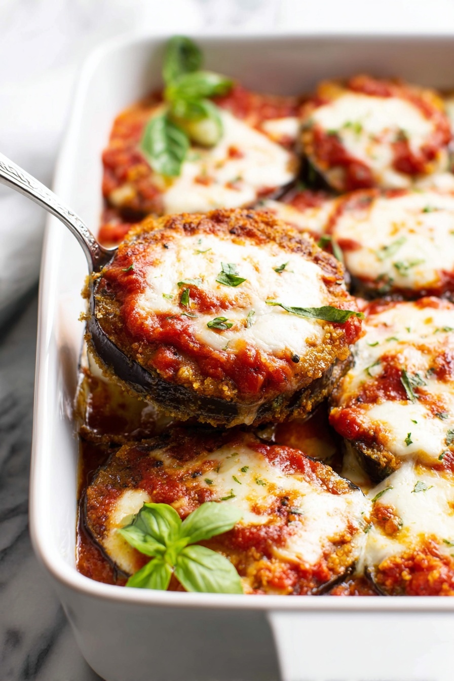 A white rectangular baking dish filled with layers of round slices of eggplant that have a brown crispy crust, covered in bright red tomato sauce with chunky texture, and thick melted white cheese that is slightly browned and bubbly on top. The eggplant slices are stacked in several layers, and fresh green basil leaves sit on one corner of the dish. A silver serving spoon is lifting one stack out, showing the layers clearly. The dish is placed on a white marbled surface. Photo taken with an iphone --ar 2:3 --v 7