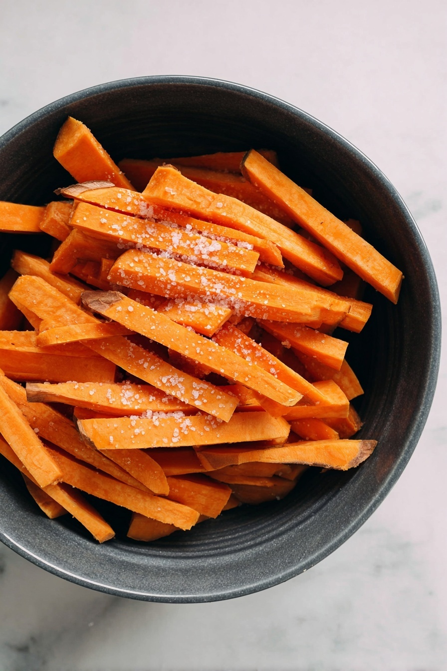A round white bowl filled with light beige dipping sauce is placed on a soft grey cloth on a white marbled surface. Around the bowl, there are several long, thin, slightly burnt orange sweet potato fries with darkened edges. Two fries are dipped into the sauce, standing upright. In the top left corner, a white bowl lined with white parchment paper holds more sweet potato fries. photo taken with an iphone --ar 2:3 --v 7