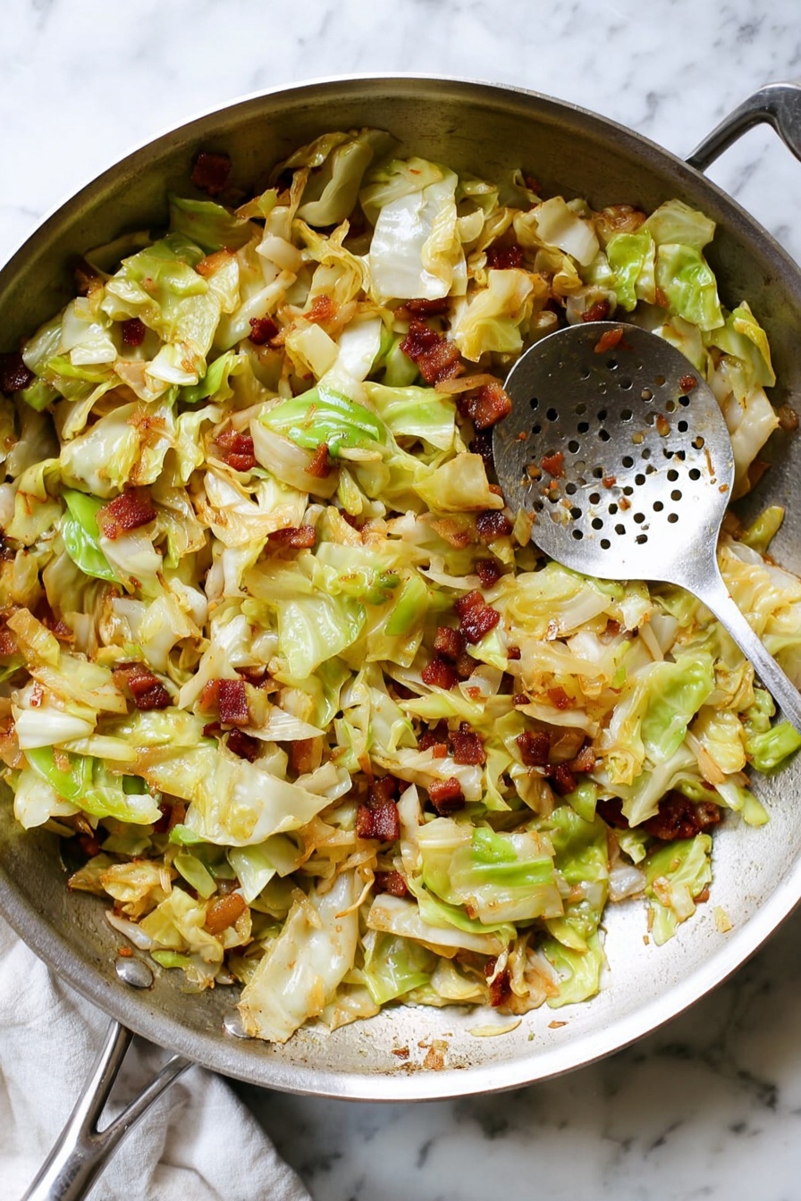 A close-up view of a large silver pan filled with cooked chopped cabbage mixed with small crispy brown pieces, likely bacon, and bits of sautéed light brown onions. The cabbage pieces are light green and pale yellow with slightly wilted edges. A silver slotted spoon rests in the pan on the right side, showing some food bits stuck to it. The pan is placed on a white marbled surface with soft natural lighting. Photo taken with an iphone --ar 2:3 --v 7