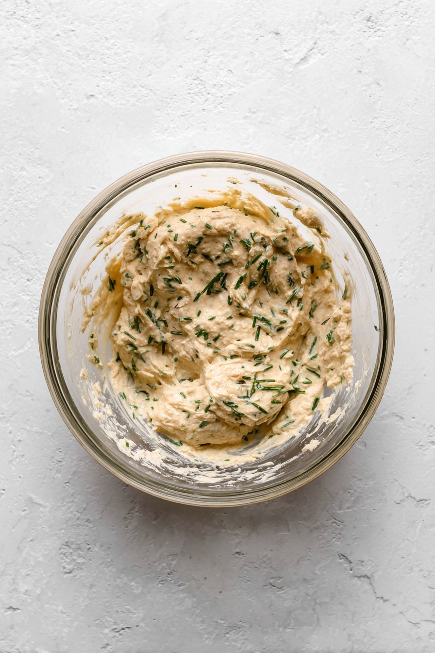 A juicy steak sliced into four thick pieces showing a pink, moist inside with a dark brown, grilled outer layer. On top of the slices is a spread of chopped garlic and herbs with a coarse texture, garnished with fresh green sprigs of rosemary. Next to the steak, a whole head of garlic adds a rustic touch, all placed on a wood cutting board with a few scattered salt grains around. The photo is taken with an iphone --ar 2:3 --v 7