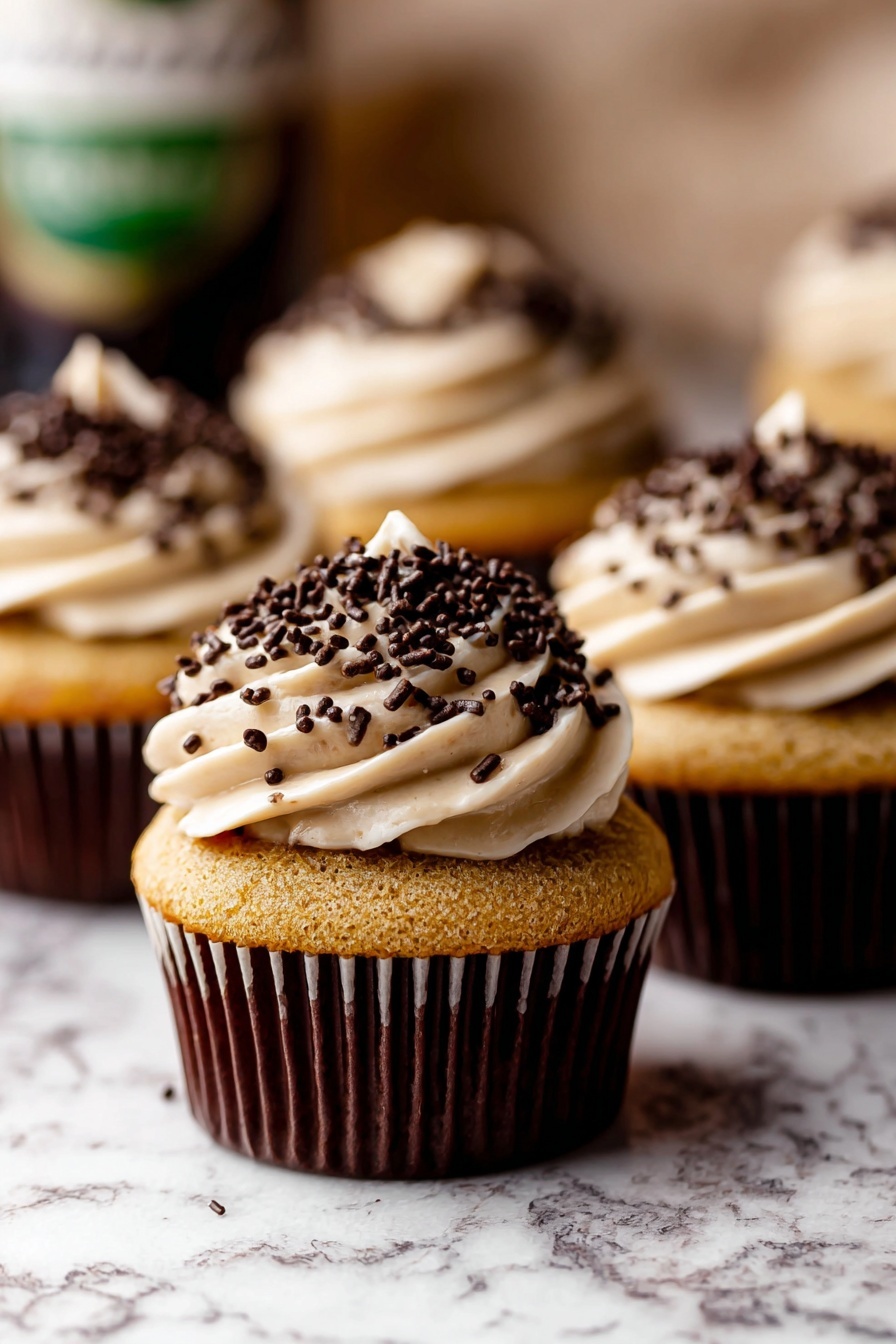 The image shows a close-up of several cupcakes with a golden brown base wrapped in dark brown liners. On top of each cupcake, there is a thick swirl of light beige frosting, generously covered with small dark chocolate sprinkles. The cupcakes are placed on a white marbled surface, and the background is softly blurred, making the cupcakes the clear focus. The frosting is smooth and creamy with a slightly peaked top. photo taken with an iphone --ar 2:3 --v 7